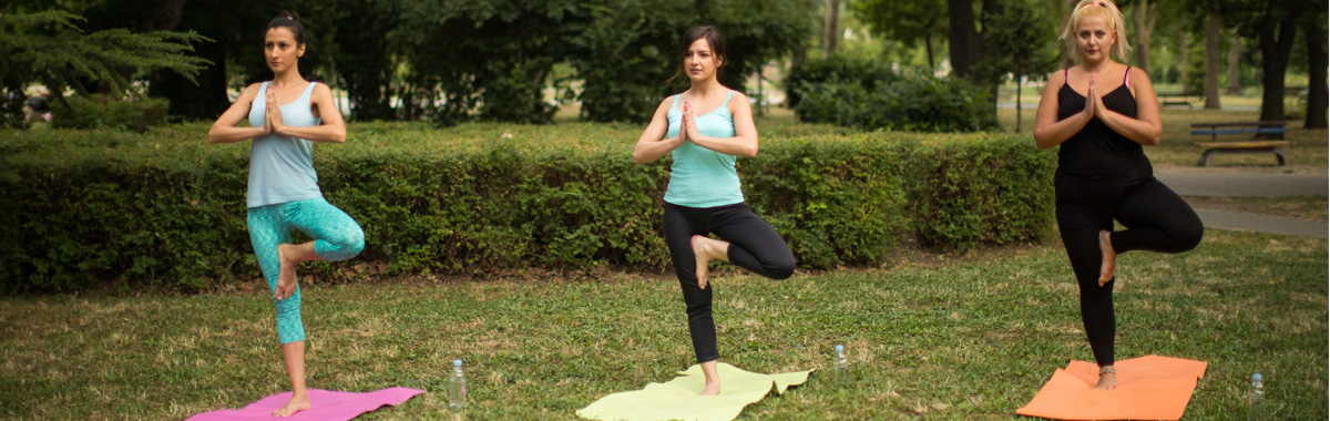 three women performing tree pose in outdoor yoga class
