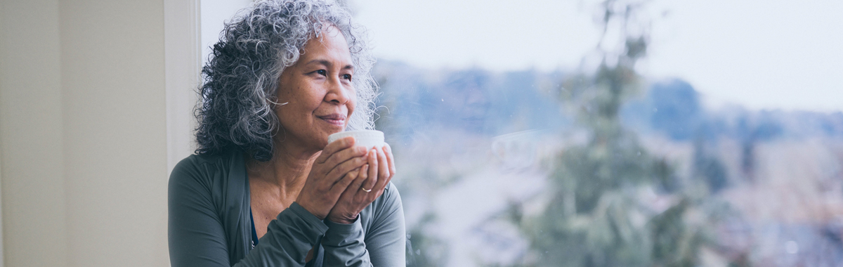 woman practicing mindfulness while holding a white mug looking out the window