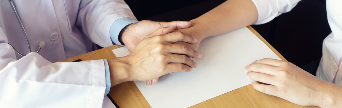 Health care provider holding a patient's hand on wooden table that has a paper on it