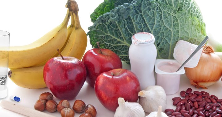 Bananas, apples, onions, yogurt, and various healthy foods along with a bottle of probiotics and a glass of water on a white surface