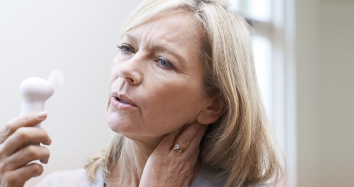 Woman going through menopause holds handheld fan in front of face