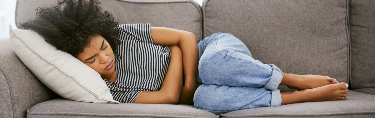 Woman lying on couch with both arms wrapped around abdomen - IBS Triggers