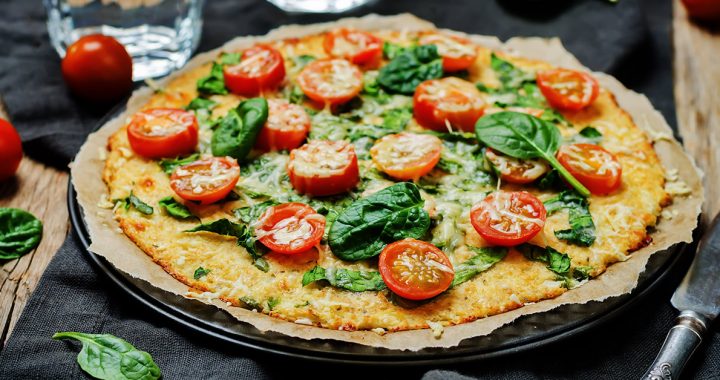Cauliflower Crust Pizza sitting on a table with spinach and tomatoes
