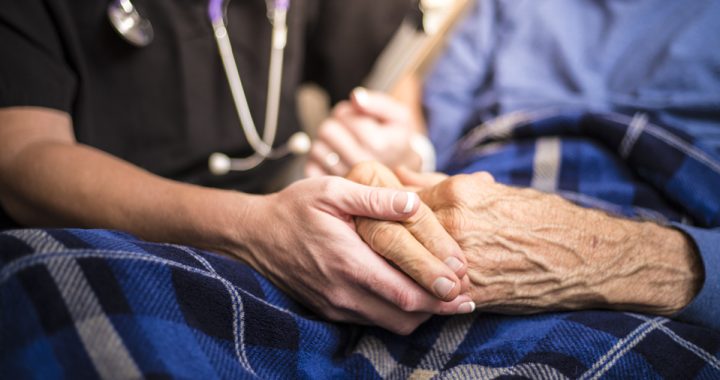 a young nurse's hand holds and elderly person's hand on their lap