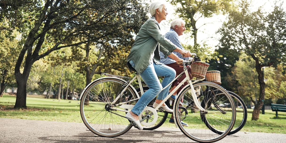 An elderly man and woman take a bike ride down a tree covered path