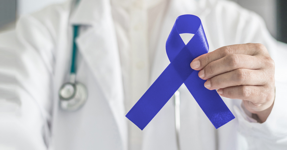 A doctor in a white coat holds a blue ribbon representing colon cancer awareness