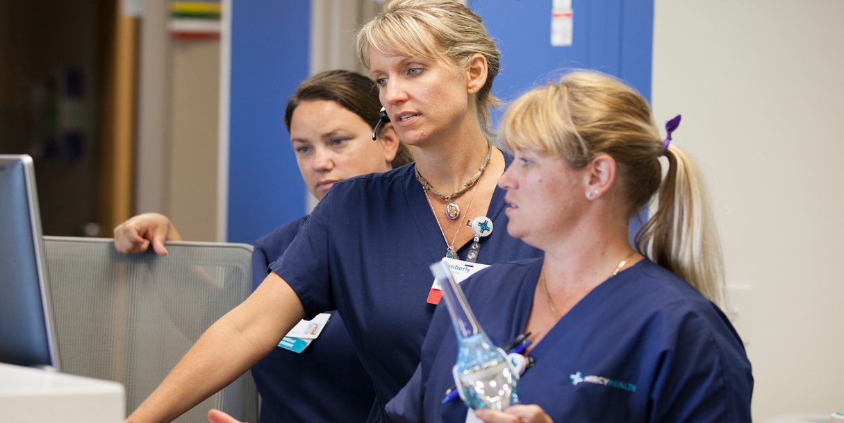 Mercy Health Nurses wearing dark blue scrubs gather around a monitor at the hospital