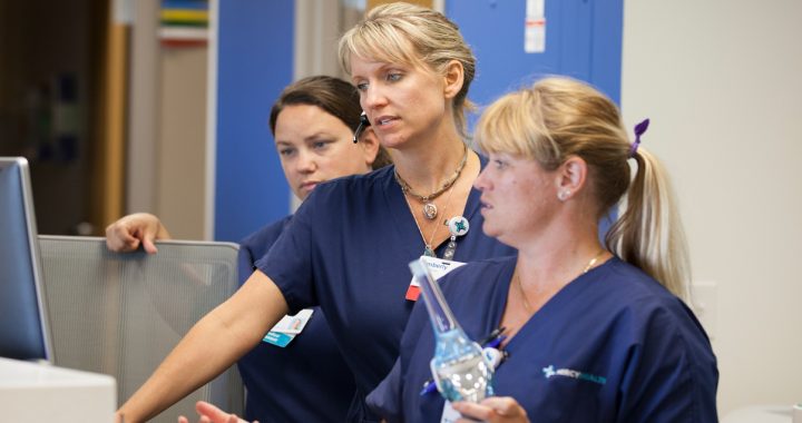 Mercy Health Nurses wearing dark blue scrubs gather around a monitor at the hospital