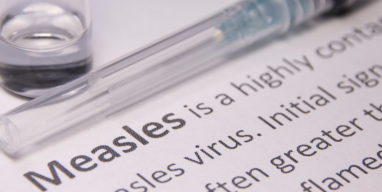 A measles vaccine lays on a sheet of paper with the definition of the measles virus.