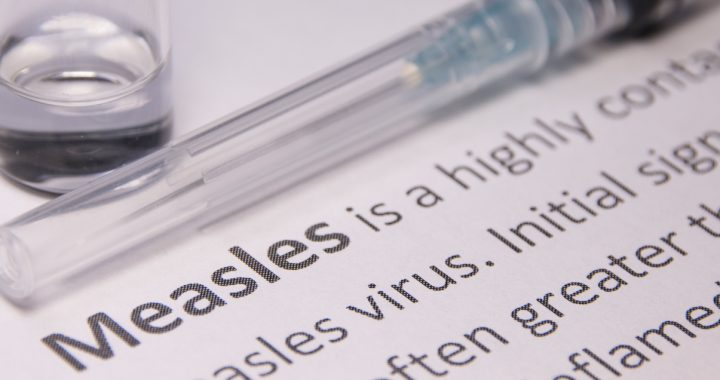 A measles vaccine lays on a sheet of paper with the definition of the measles virus.