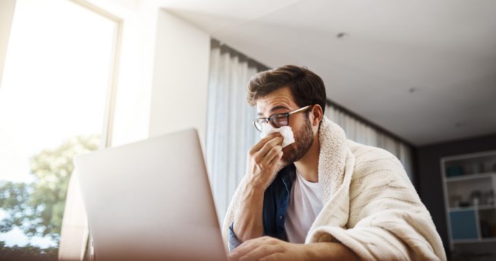 Man wiping his noes while looking at computer.