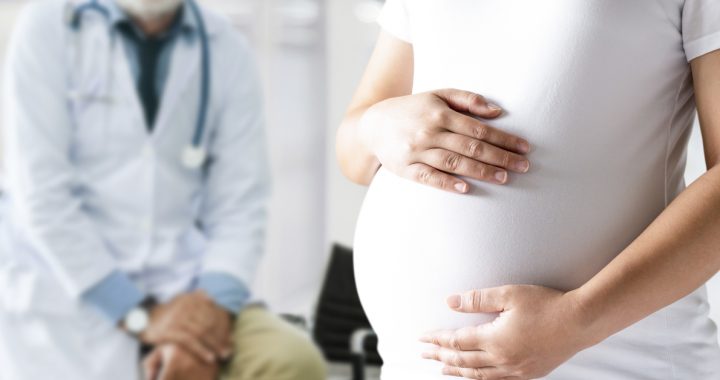 Pregnant women holding her baby bump with a physician in the background.