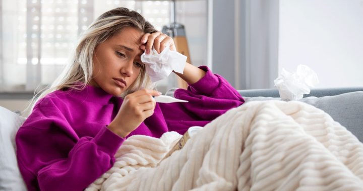 A woman checking her temperature, fever is a common COVID-19 symptom.