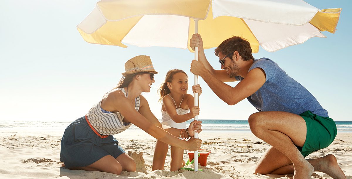 A family using an umbrella at the beach to protect themselves from the sun and UV rays.