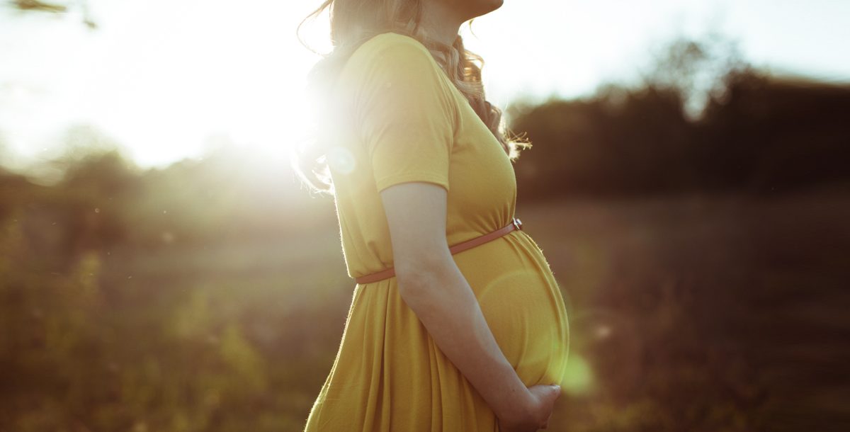 Woman holding her baby bump with sunshine in the background.