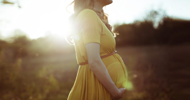 Woman holding her baby bump with sunshine in the background.